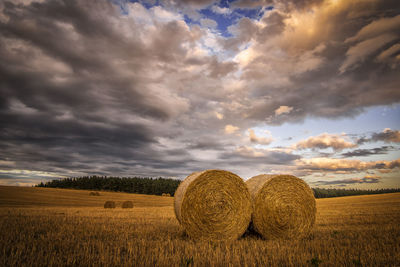 Hay bales on field against cloudy sky