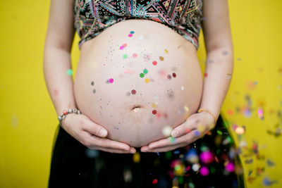 Midsection of pregnant woman against yellow background