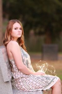 Portrait of beautiful woman holding illuminated string lights while sitting on bench