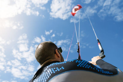 Rear view of man holding kiteboard against sky