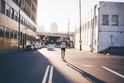 Man skateboarding on city street against sky during sunny day