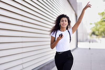 Young woman listening music while walking on footpath by wall