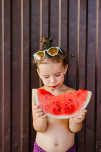 Shirtless girl eating watermelon against wall