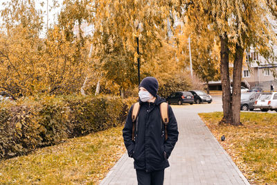 Boy wearing mask standing on footpath during autumn