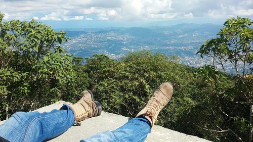 Low section of man relaxing by trees against sky