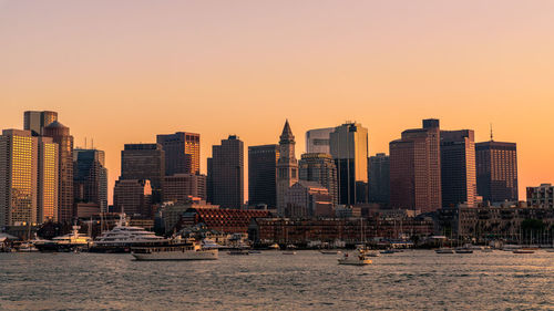 Modern buildings by sea against clear sky during sunset