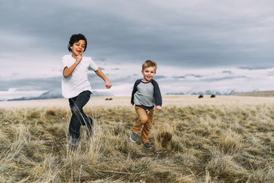 Brothers running while playing on grassy field against cloudy sky