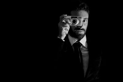 Man photographing from camera while standing against black background