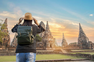 Rear view of woman with backpack standing at temple against sky during sunset