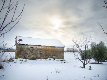 Snow covered field by building against sky