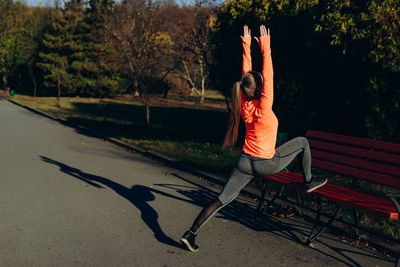 Young fitness girl doing stretching while leaning on a bench before running outdoor in the park