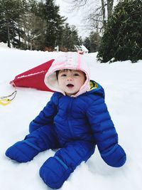 Portrait of cute baby boy wearing warm clothing sitting in snow
