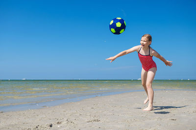 Full length of woman ball on beach against blue sky