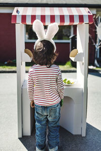 Rear view of boy standing at artificial concession stand on footpath