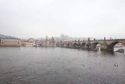 Bridge over river by buildings against clear sky