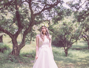 Portrait of young woman in dress standing against trees