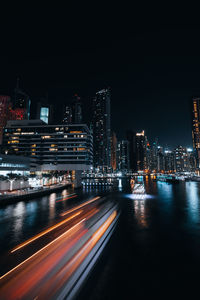 Illuminated city by river against sky at night