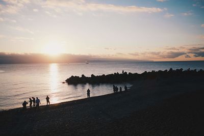 People on beach against sky during sunset