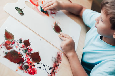 Cute child sitting at desk and making picture from dry birch leaves. autumn activities for children