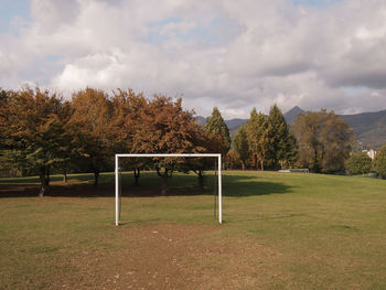 Empty bench on field by trees against sky