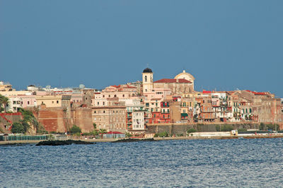 Buildings by sea against clear blue sky