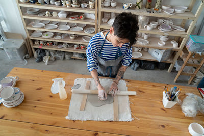 Creative successful woman ceramist applying pattern on clay decorating ceramic item in workshop
