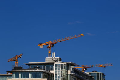 Low angle view of crane by building against clear blue sky