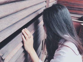 Side view of young woman peeking through wooden window shutters