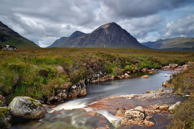 Scenic view of stream by mountains against sky