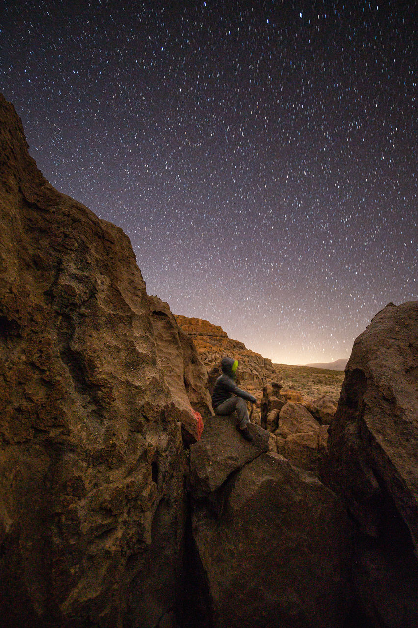 REAR VIEW OF PERSON ON ROCK AGAINST SKY