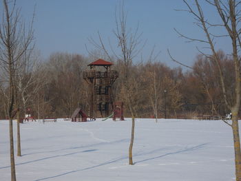 Bare trees on snowy field against sky during winter