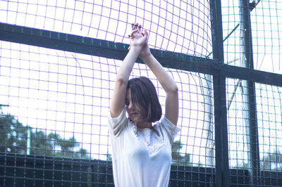 Woman with arms raised against chainlink fence