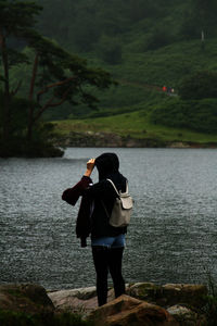 Rear view of woman standing by lake in rain with hood on in peak district, england, united kingdom