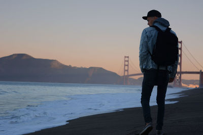 Rear view of man walking against golden gate bridge during sunset