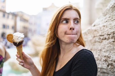 Millennial redhead woman eating ice cream on city street