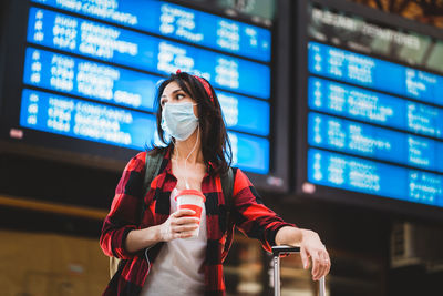 Young woman wearing mask looking away while standing at airport