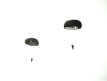 Low angle view of men with parachutes against clear sky