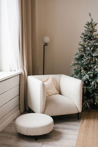 White armchair and ottoman are in front of a christmas tree at living room