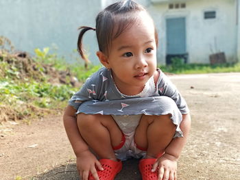 Cute baby girl looking away while crouching on road