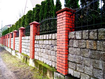 Red brick wall by trees against sky