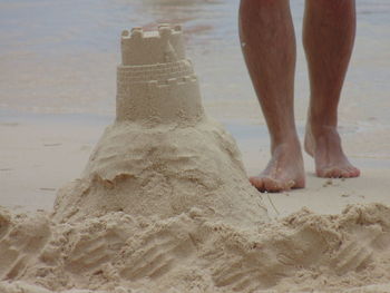 Low section of man standing on sand at beach