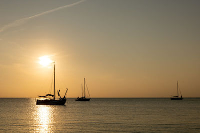 Silhouette sailboats in sea against sky during sunset