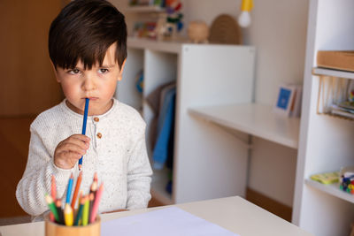 Cute boy holding colored pencil at home