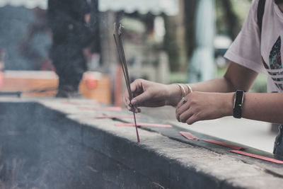 Cropped image of woman placing lit incense stick on railing