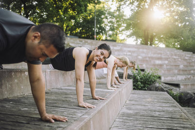 Portrait of smiling woman doing push-ups with friends on steps at park