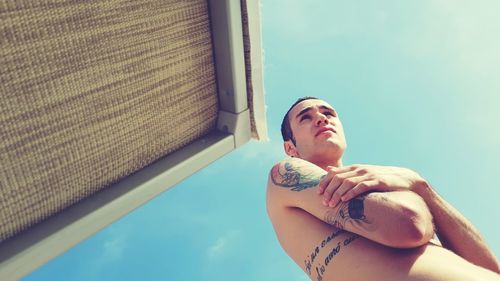 Low angle view of shirtless man standing against sky on sunny day