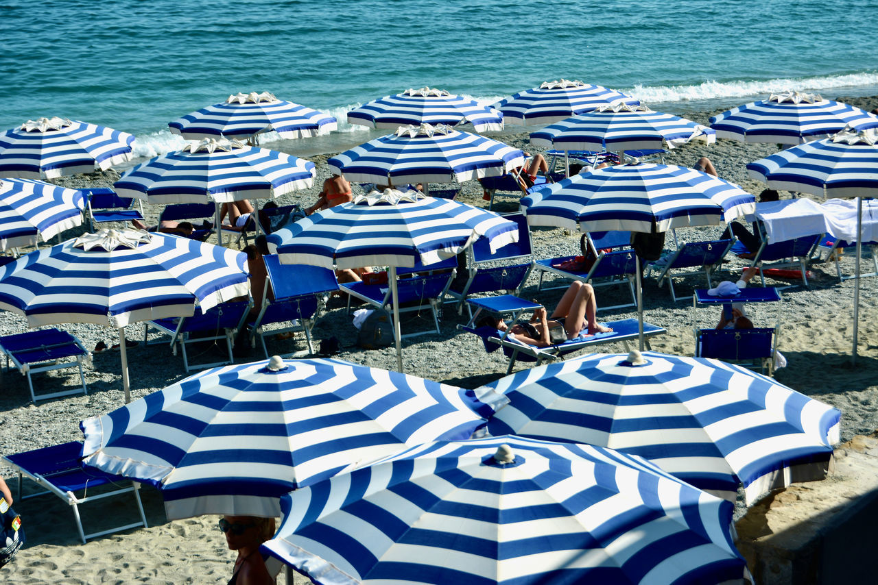 umbrella, water, parasol, beach, sea, chair, land, high angle view, nature, beach umbrella, day, protection, seat, sunlight, sunshade, relaxation, vacation, trip, travel destinations, holiday, lounge chair, in a row, no people, outdoors, sand, shade, striped, deck chair, table, security, beauty in nature, tourism, travel, large group of objects, arrangement, nautical vessel, fashion accessory