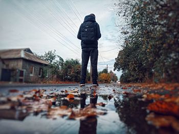 Rear view of man standing on puddle during rainy season