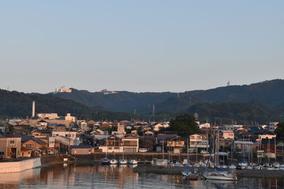 Sailboats moored on harbor by buildings against sky