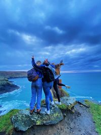 Full length of friends standing on rock by sea against sky